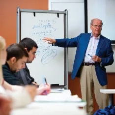 A man in a suit delivering a lecture to a group of students.